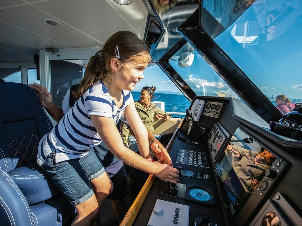 Excited young girl at helm of boat next to boat skipper