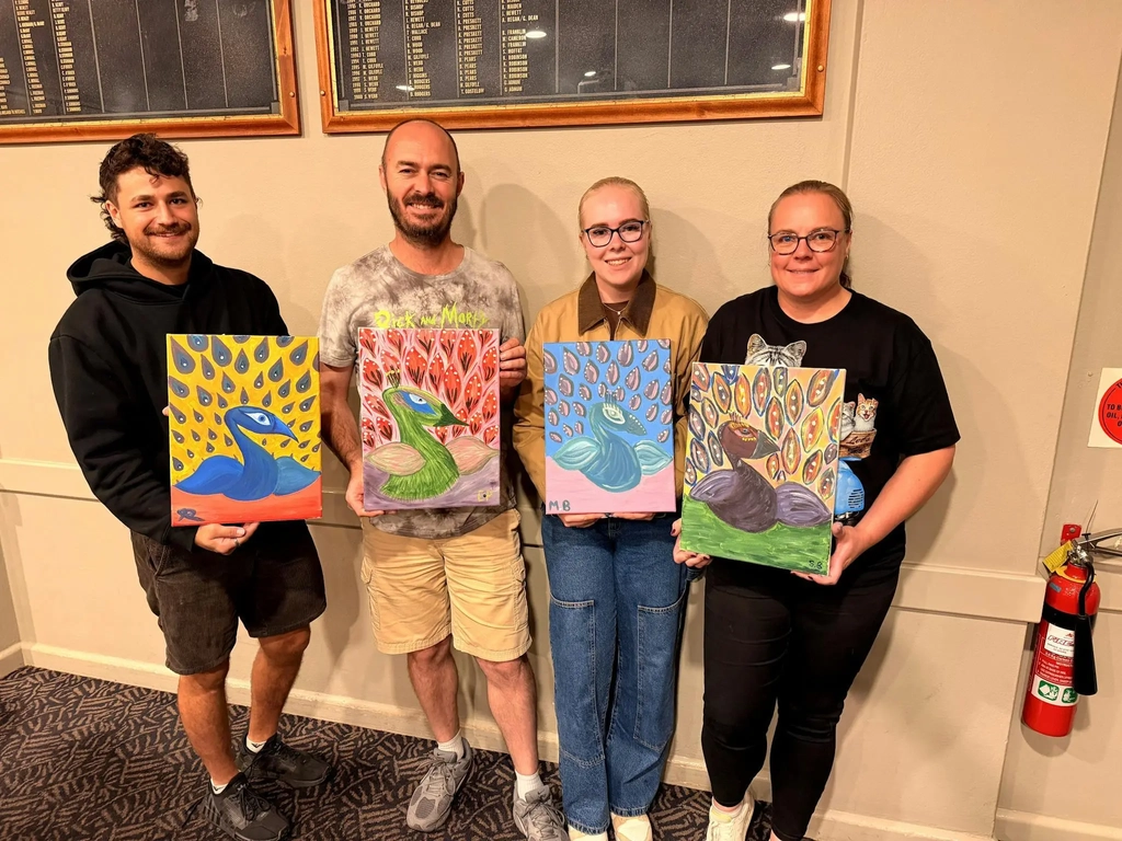 Group of Paint Juicy guests holding their finished peacock paintings at a mobile paint and sip event