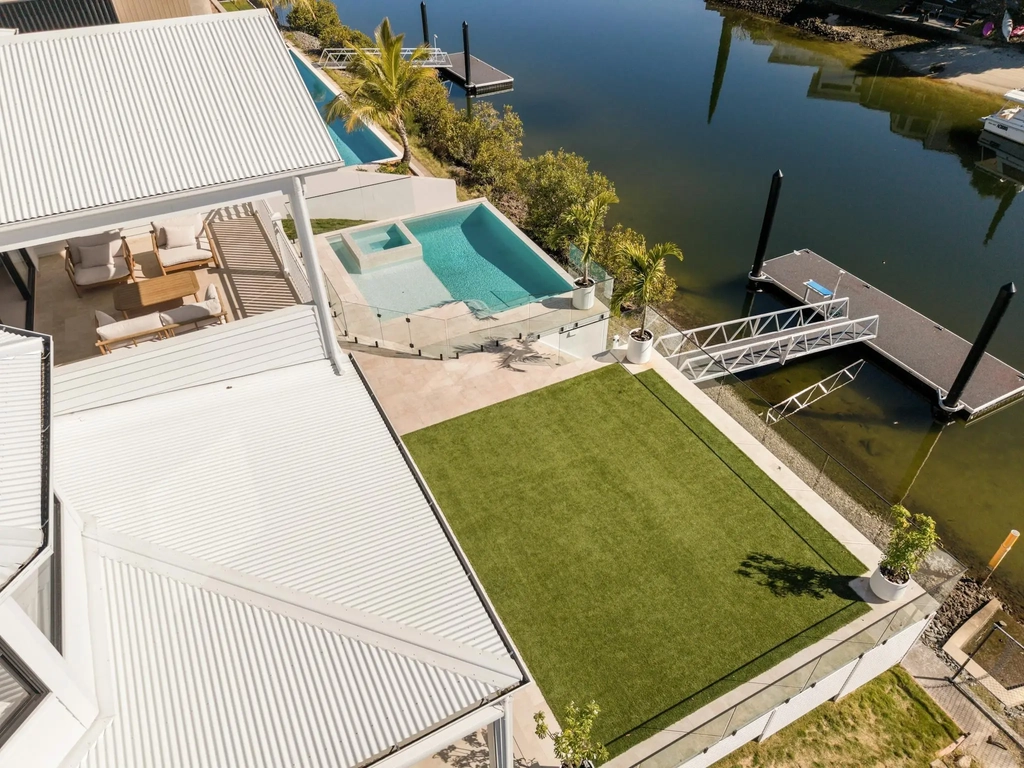 Aerial view of a swimming pool, spa, lawn and private pontoon on a canal
