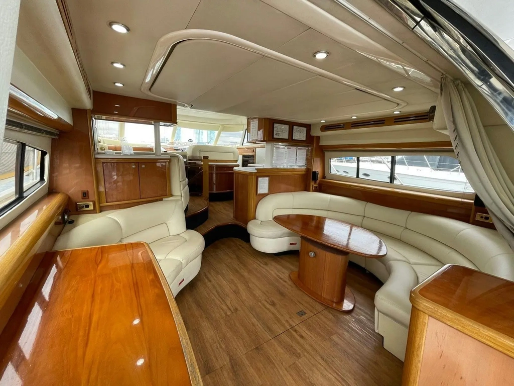 Luxury yacht interior showing curved leather lounge seating, dining table, and polished timber cabin