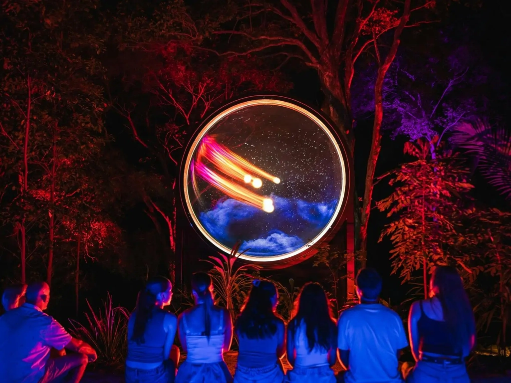 Group of people sitting on bench watching a colourful light spectacle inside a round circle.