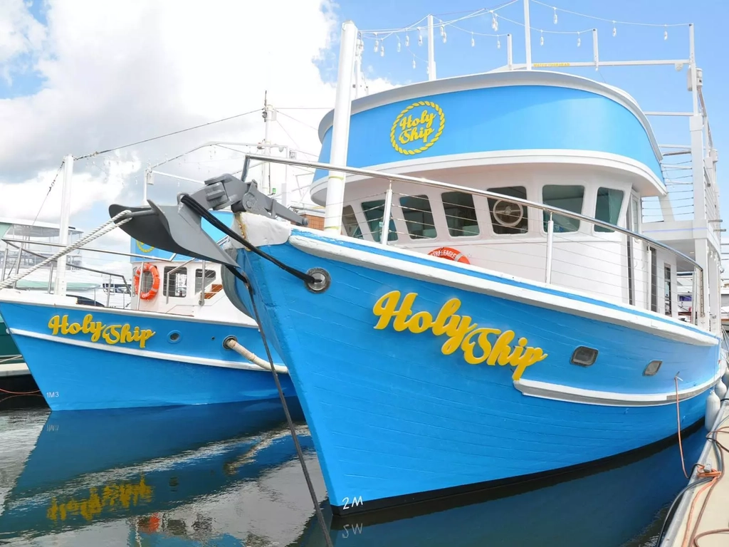 two blue trawlers transformed into a restaurant with yellow signage reading Holy Ship