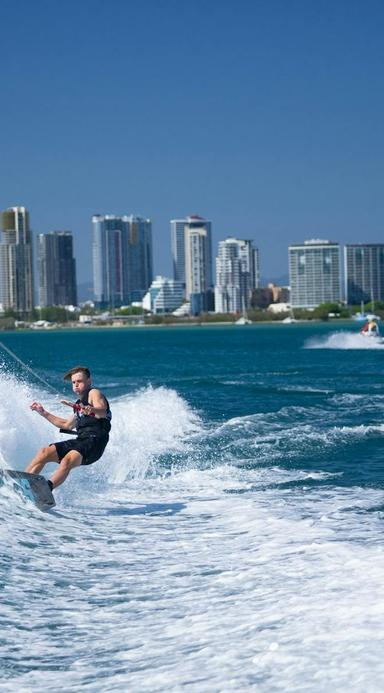 Wake boarder carving the wake with hise rise skyline in the background.