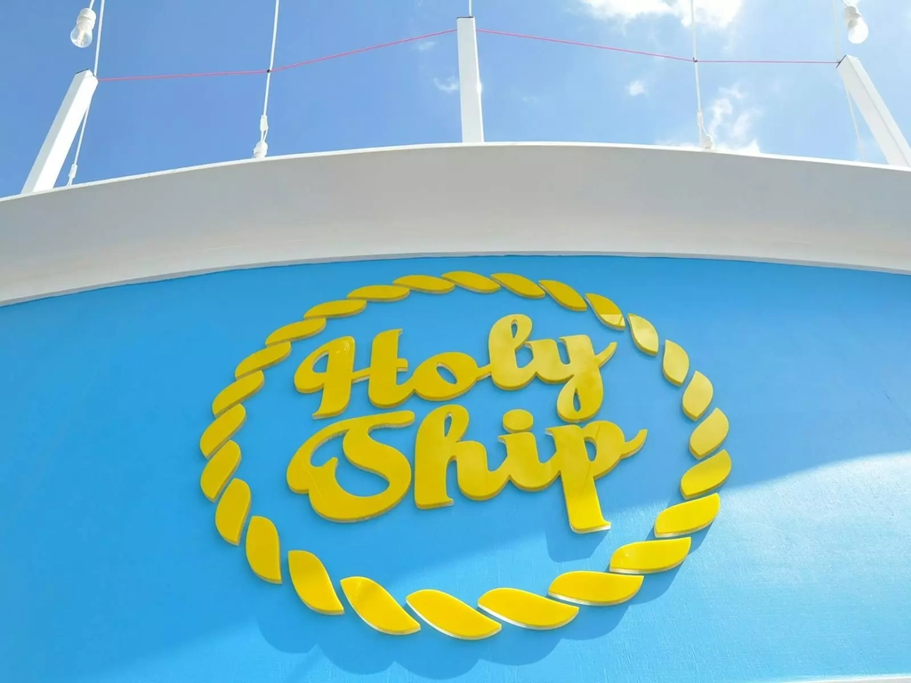 a yellow sign reading Holy Ship on the front of a blue trawler