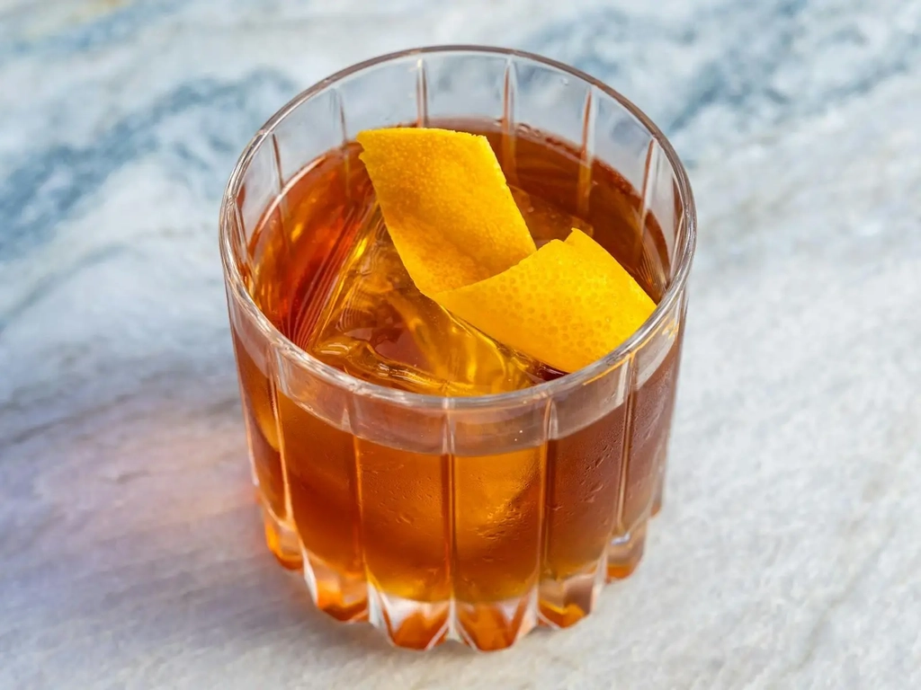 Old fashioned cocktail with orange peel in a ribbed glass on a marble bar