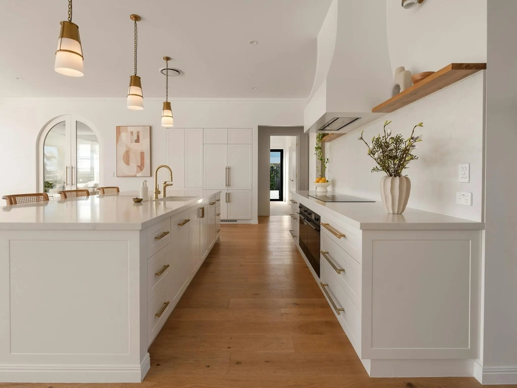 White kitchen with a long stone island, brass pendant lights and an arched doorway
