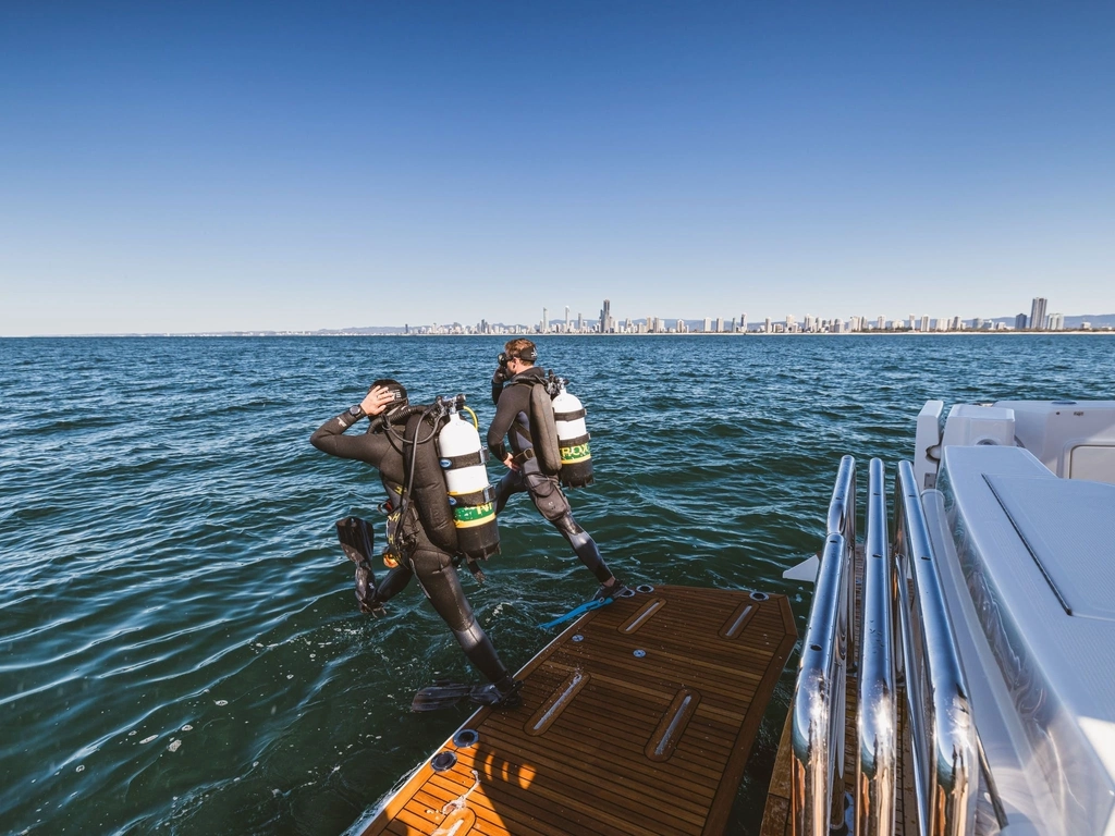 two scuba divers step off the back platform of a boat ready to dive Wonder Reef