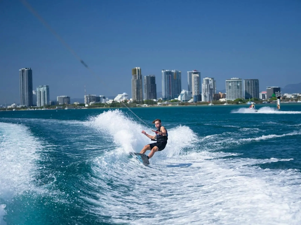 Wake boarder carving the wake with hise rise skyline in the background.