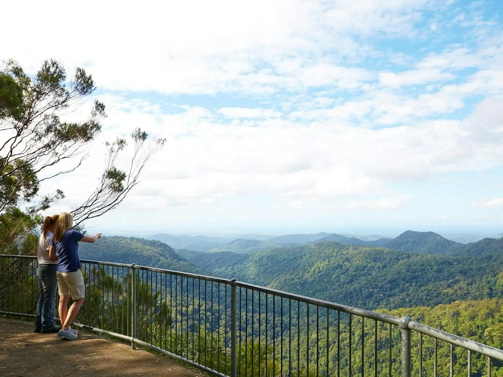 Two people standing at a lookout looking over a valley to the coast.