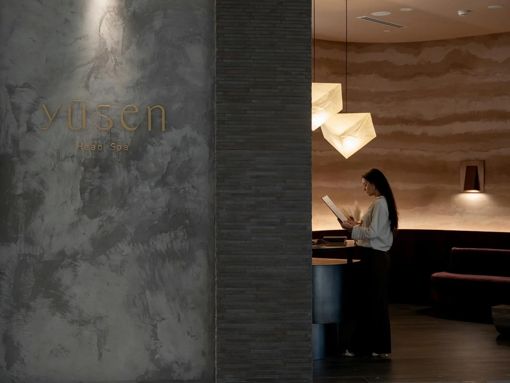 The Yūsen Head Spa reception area featuring the gold logo on a textured stone wall, warm pendant
