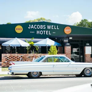 A vintage white Cadillac parked in front of the dark green Jacobs Well Hotel building on a sunny day