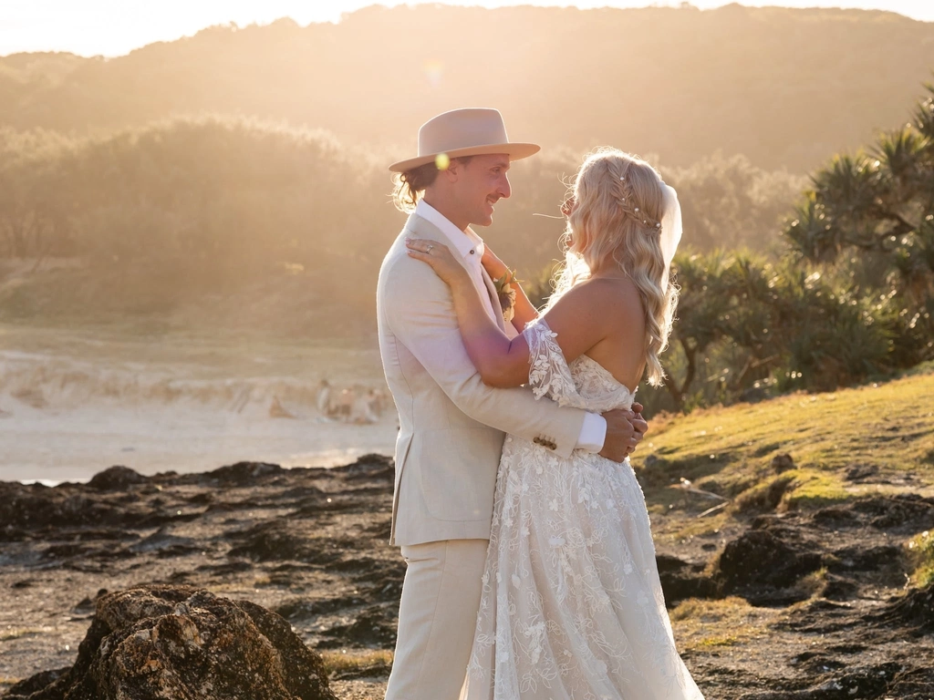 newly wed couple standing on a rocky headland with the sun setting in background