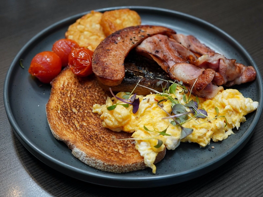 A breakfast order with bacon, sausage, scrambled eggs, hash browns, tomatoes and toast