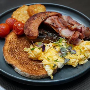 A breakfast order with bacon, sausage, scrambled eggs, hash browns, tomatoes and toast