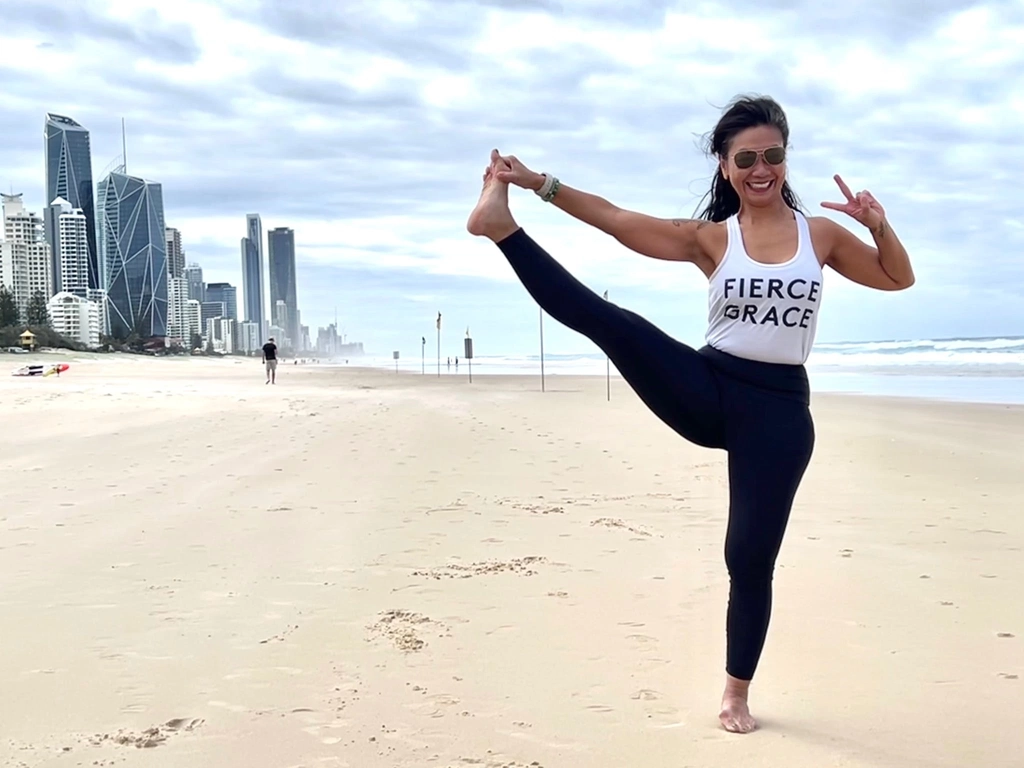 Director and Head Teacher, Rozlynn Hobbs yoga pose on the beach with Surfers skyline background.