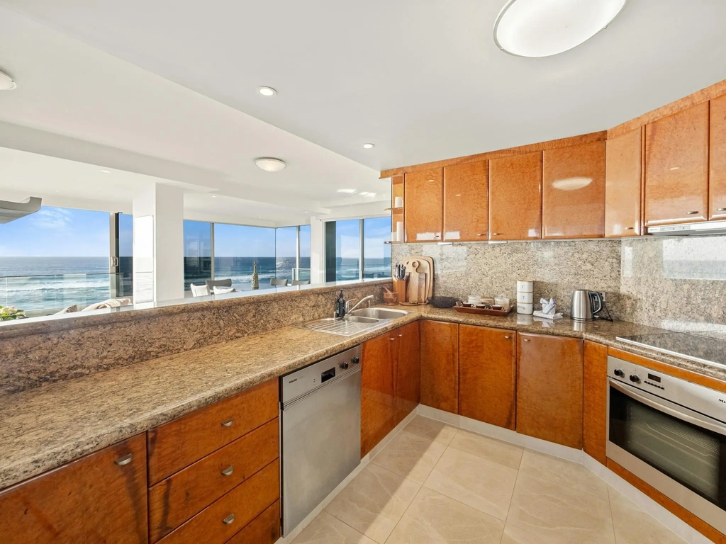 Apartment kitchen with granite benchtops and timber joinery facing the sea