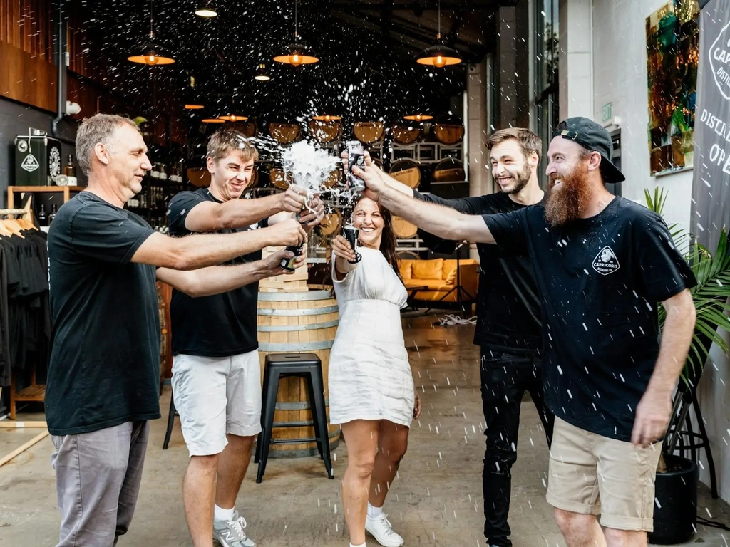 Staff celebrating and toasting with drinks, outside the distillery.