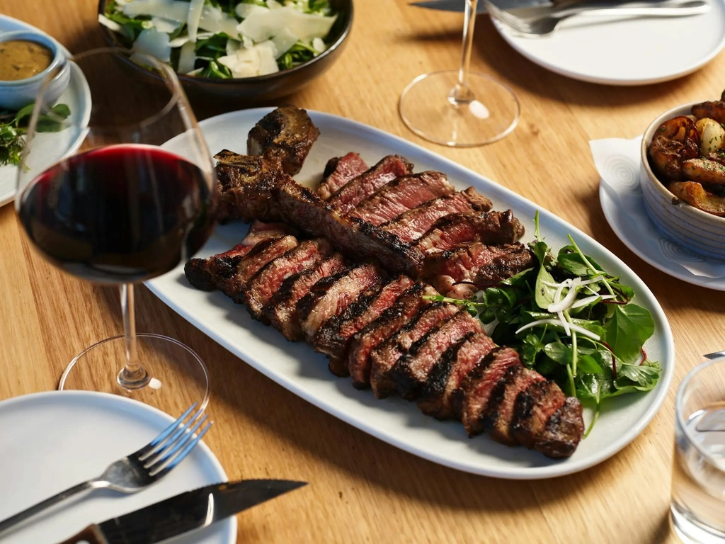 Juicy premium T-Bone steak on white plate with salad and glass of red wine at Hurricane's Grill.