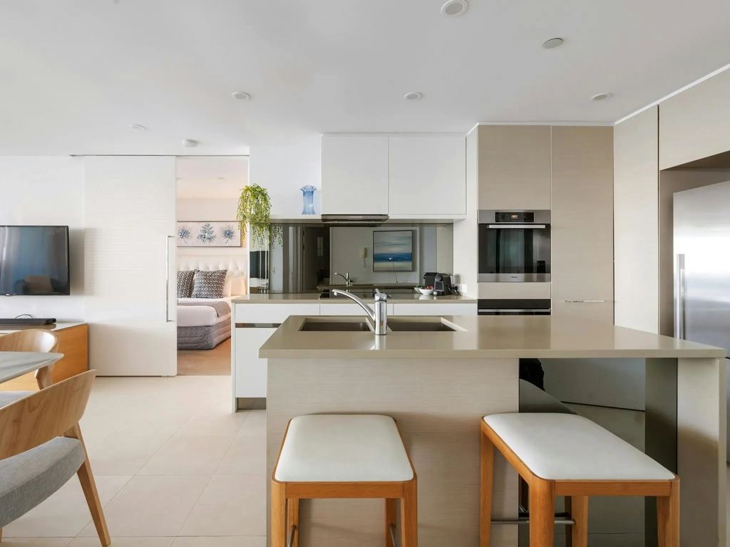 Kitchen with a stone island, bench stools, wall ovens and a tall refrigerator.