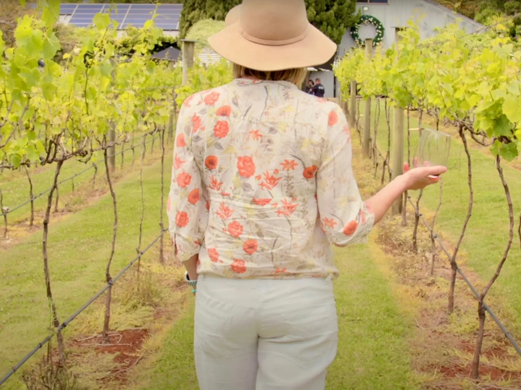 A women holding a glass of white wine walking through the vineyard at Witches Falls Winery