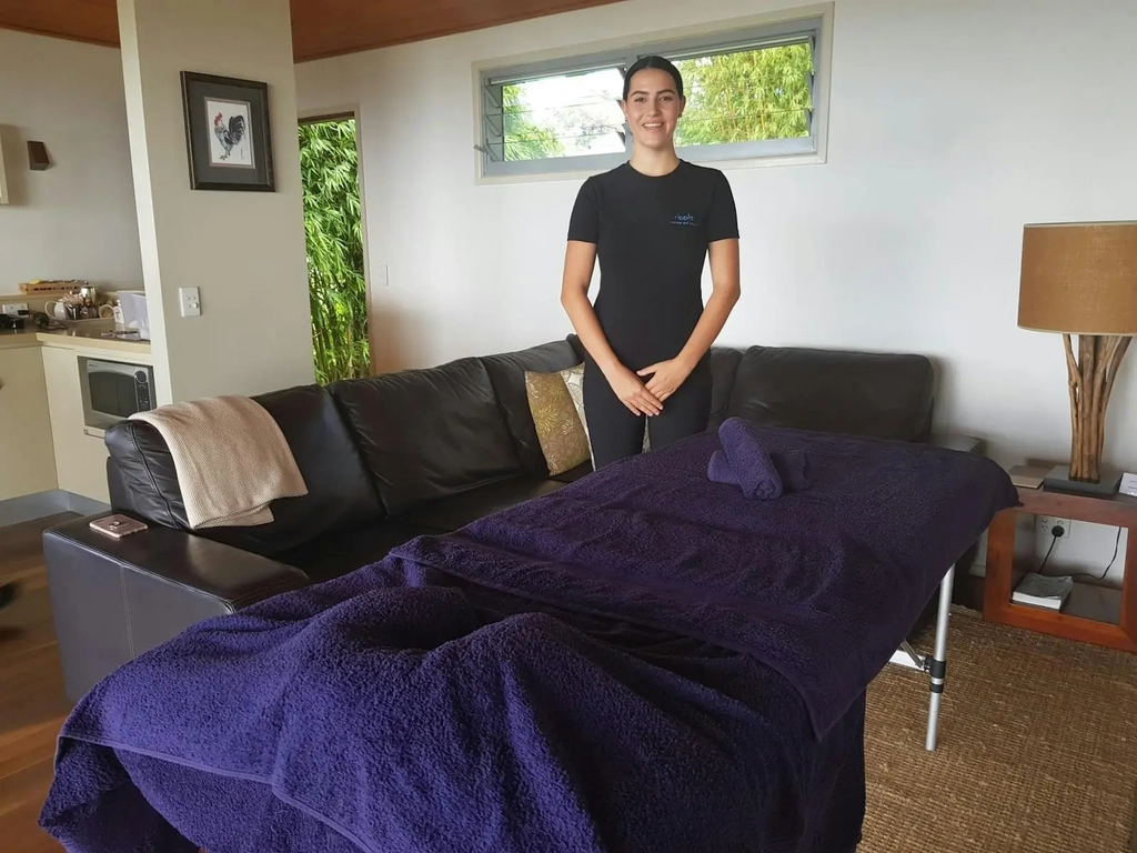 Ripple Massage therapist standing behind mobile massage table with blue towels in Gold Coast Airbnb