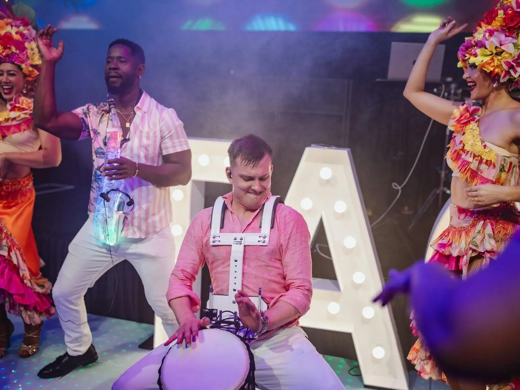 A roving drummer plays drums on the dancefloor with  LED saxophone player and two female performers