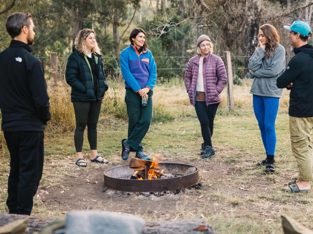 A group of people stand around a campfire, chatting