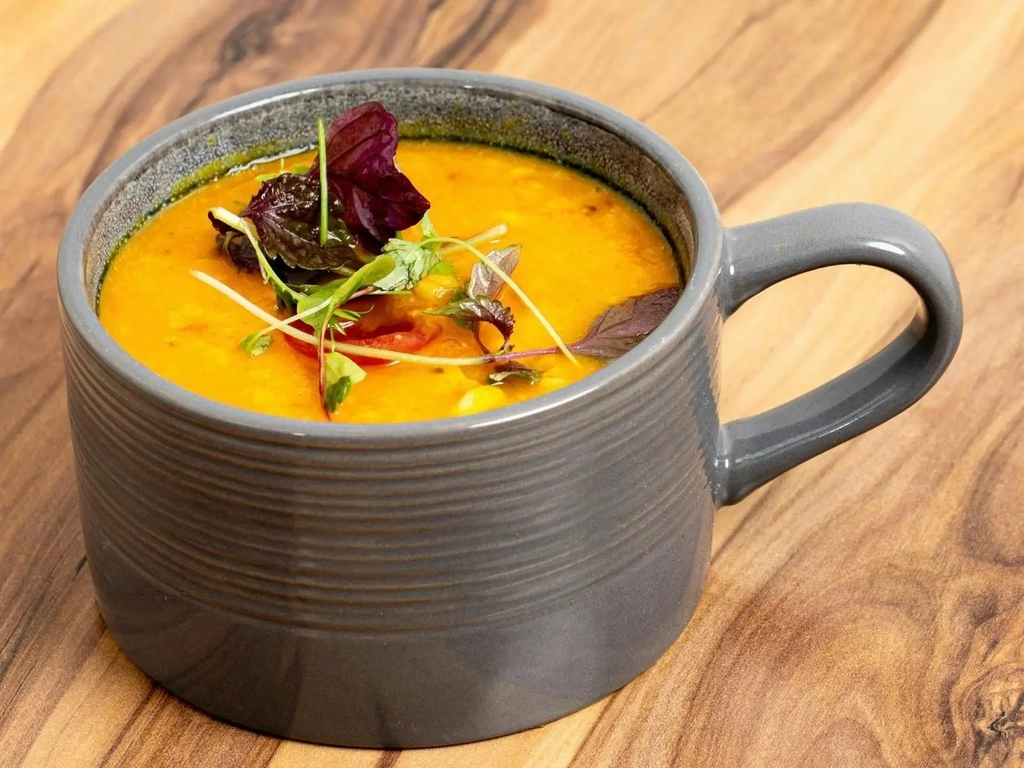 A bowl of golden Indian curry garnished with fresh herbs served on a wooden table