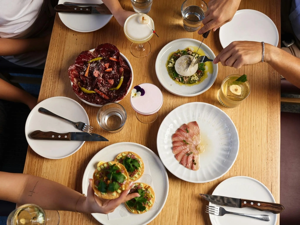 Plates of Hurricane's Surfers Paradise kingfish, tuna tostada, wagyu bresaola & burrata with drinks.