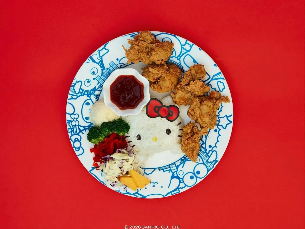 A Hello Kitty-shaped rice ball served with fried chicken, vegetables, and sauce on a plate.