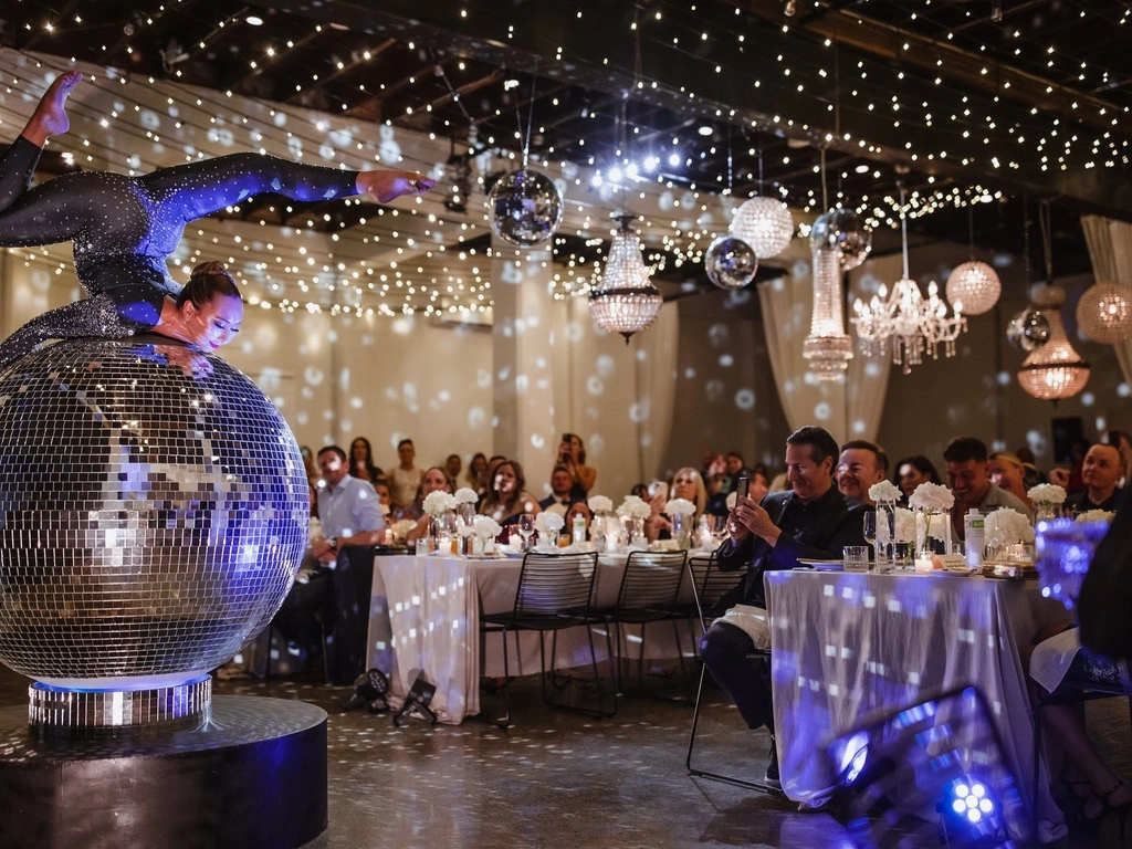 2 meter Disco Ball sits on the floor with a contortionist doing a back bend on top of it.