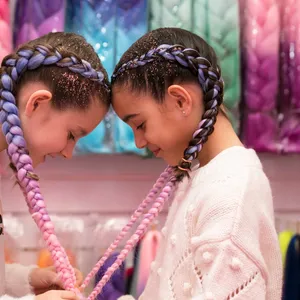 two girls with their heads together and their hair braids are forming a love heart shape