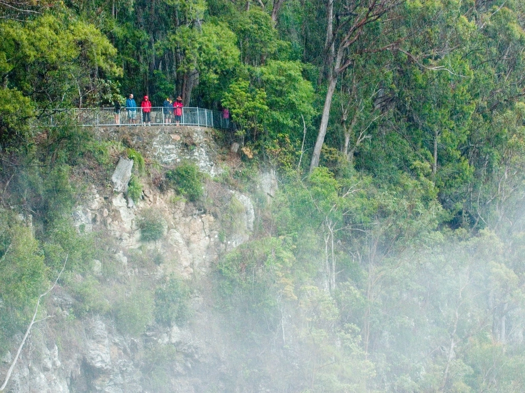People standing on lookout on cliff face shrouded in mist from the falls.