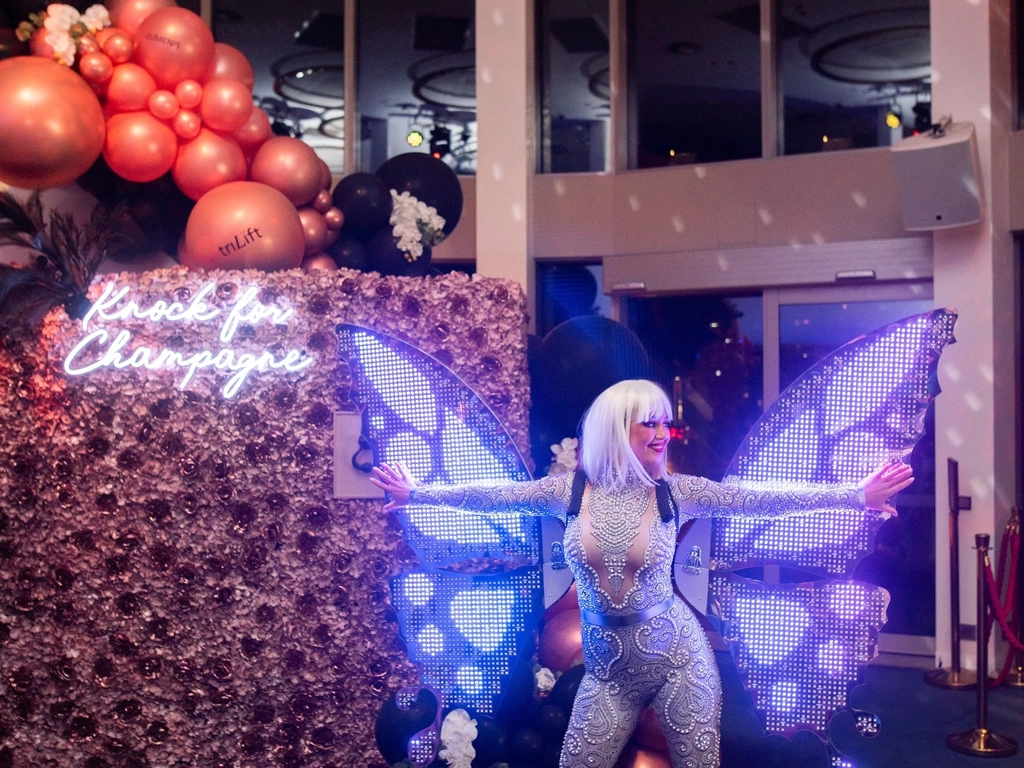 A performer wears a silver unitard costume and has giant LED wings on her shoulders.