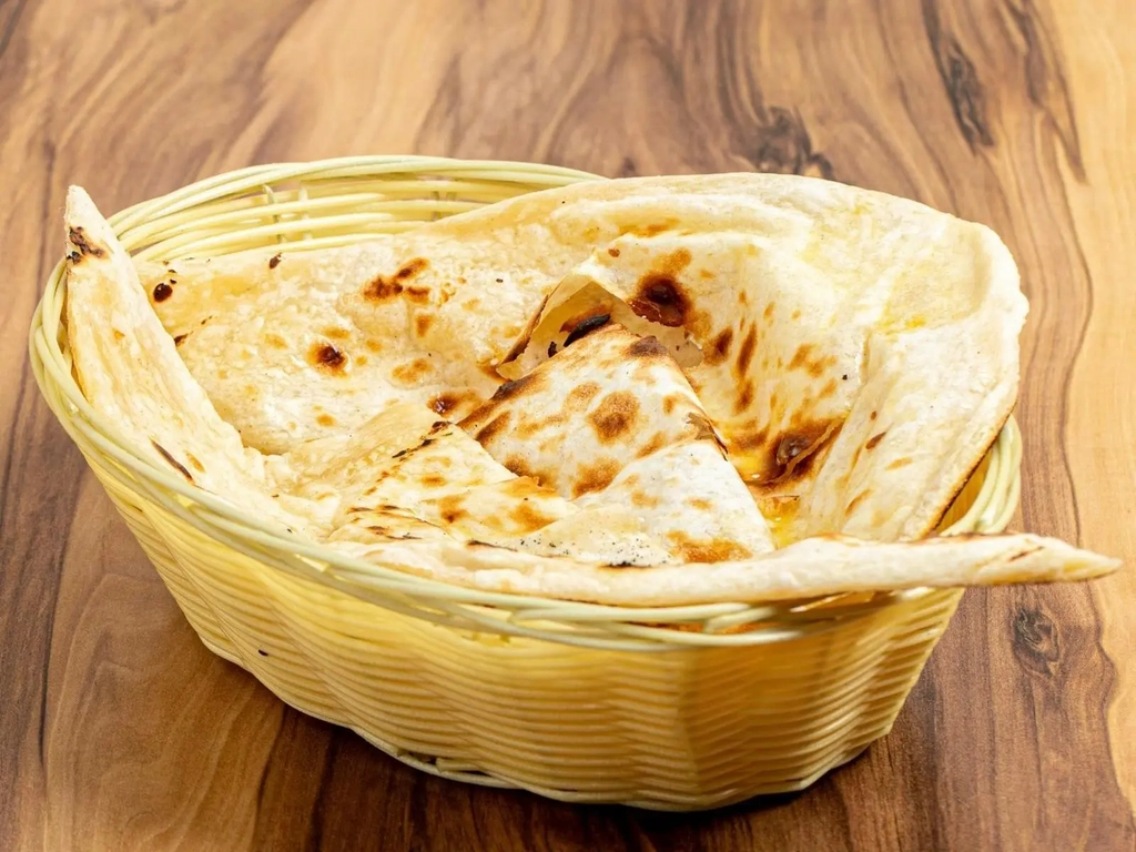 A basket of freshly baked golden naan bread on a wooden table
