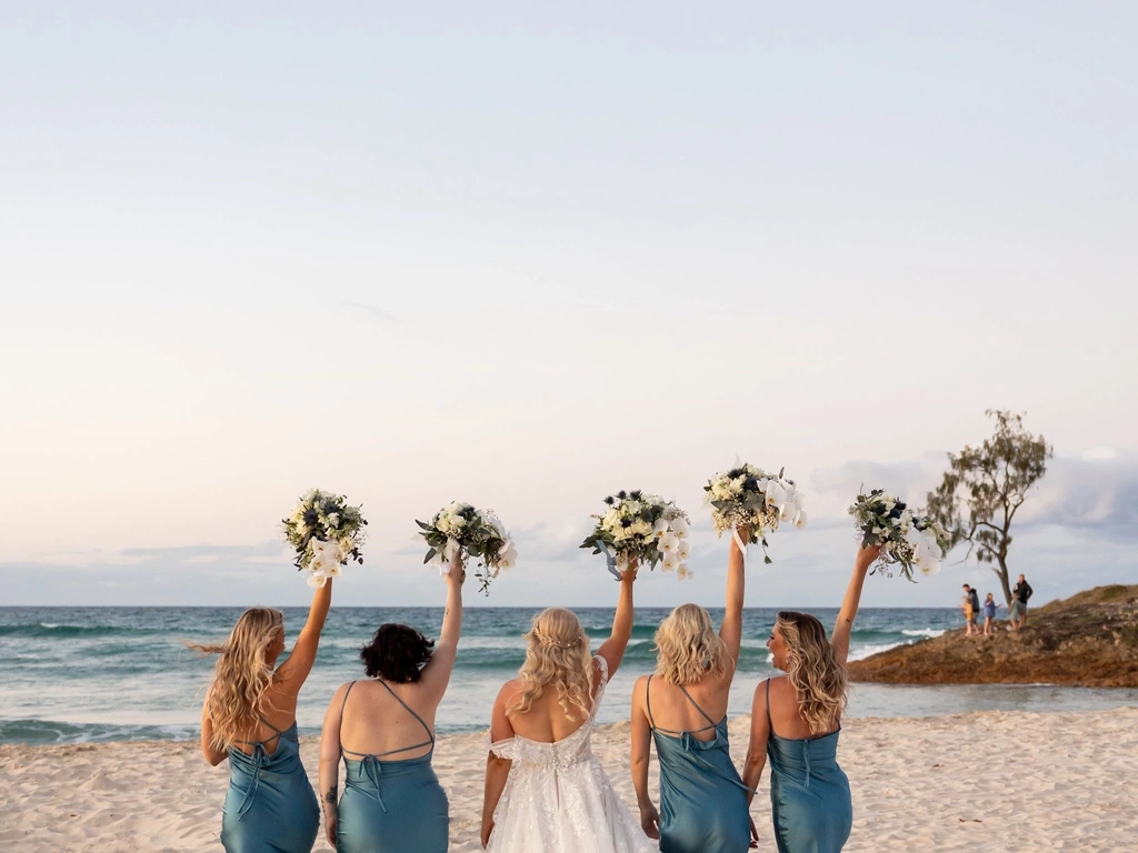 four bridesmaids in blue silk dresses and bride looking out to the ocean