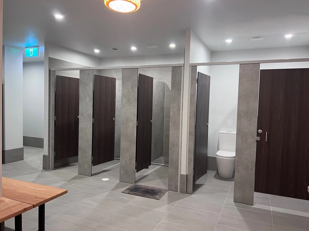 Spacious shower/changing room with concrete effect tiled floor and dark wood cubicle doors