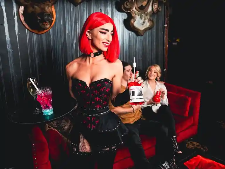 A female waitress in gothic costume serves cocktails to a male and female customer.