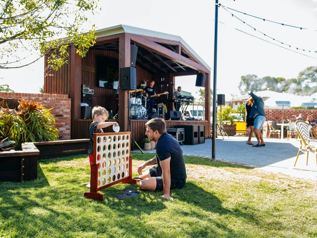 A young boy and a man play a game on a sunny lawn while a live band performs on stage
