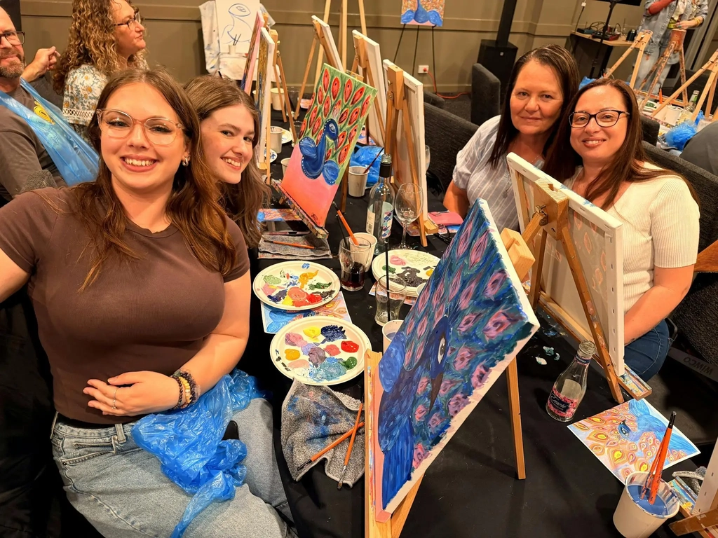 Group of Paint Juicy guests holding their finished peacock paintings at a mobile paint and sip event