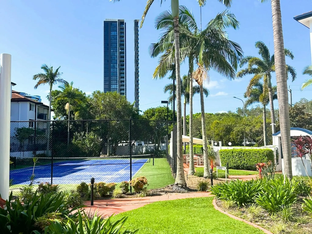 View through the green grass, trees to the tennis court