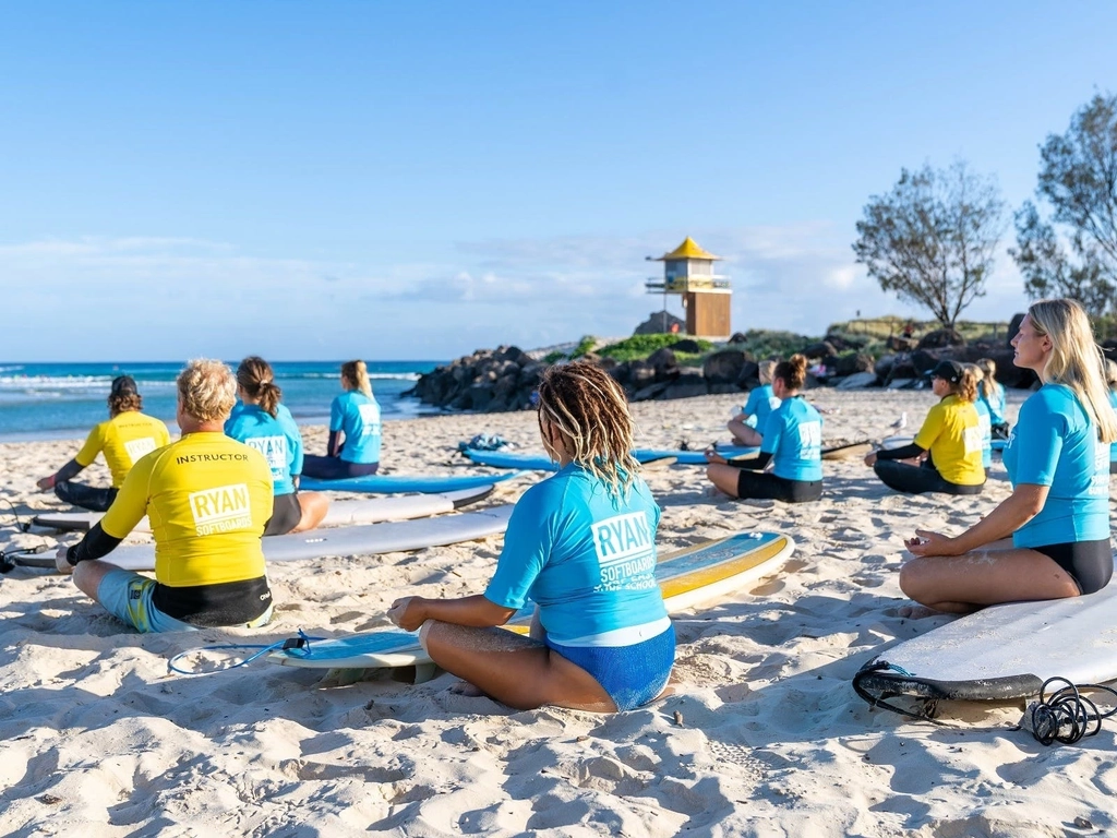 Surf school group meditating on beach.