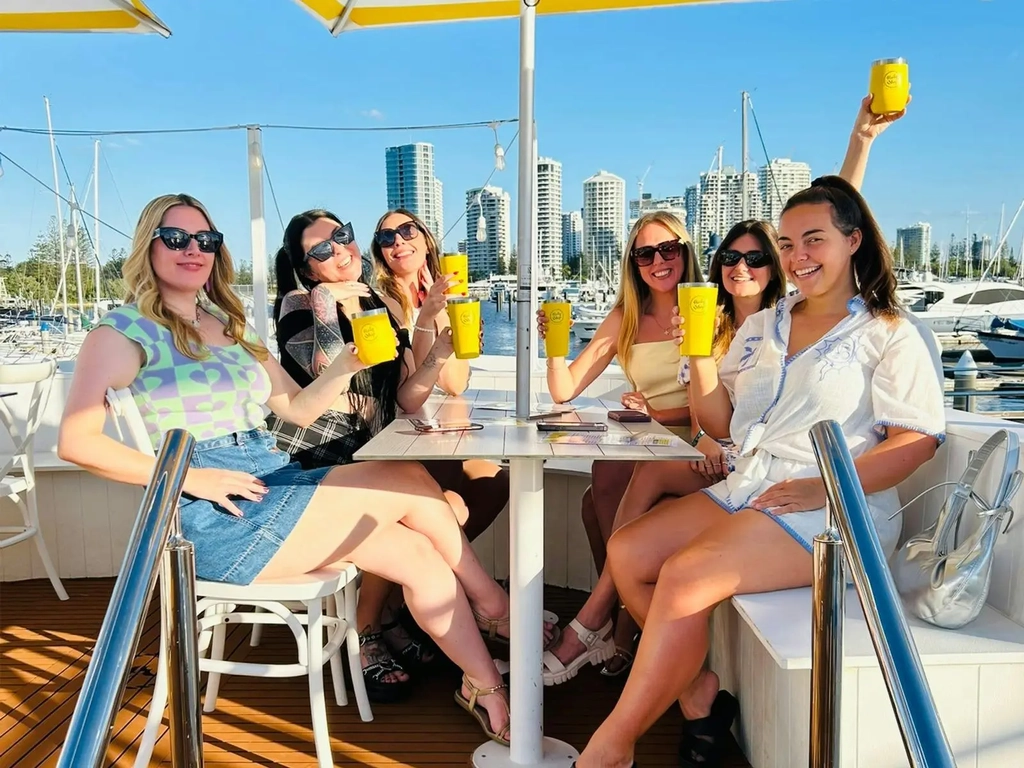 6 women dining at Holy Ship under an umbrella holding up their bright yellow cups