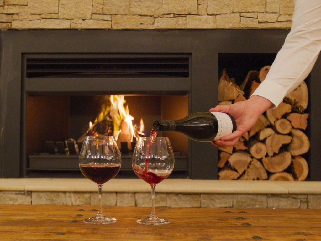 A waiter pours a glass of red in front of a roaring stone fireplace at Hazelwood Estate