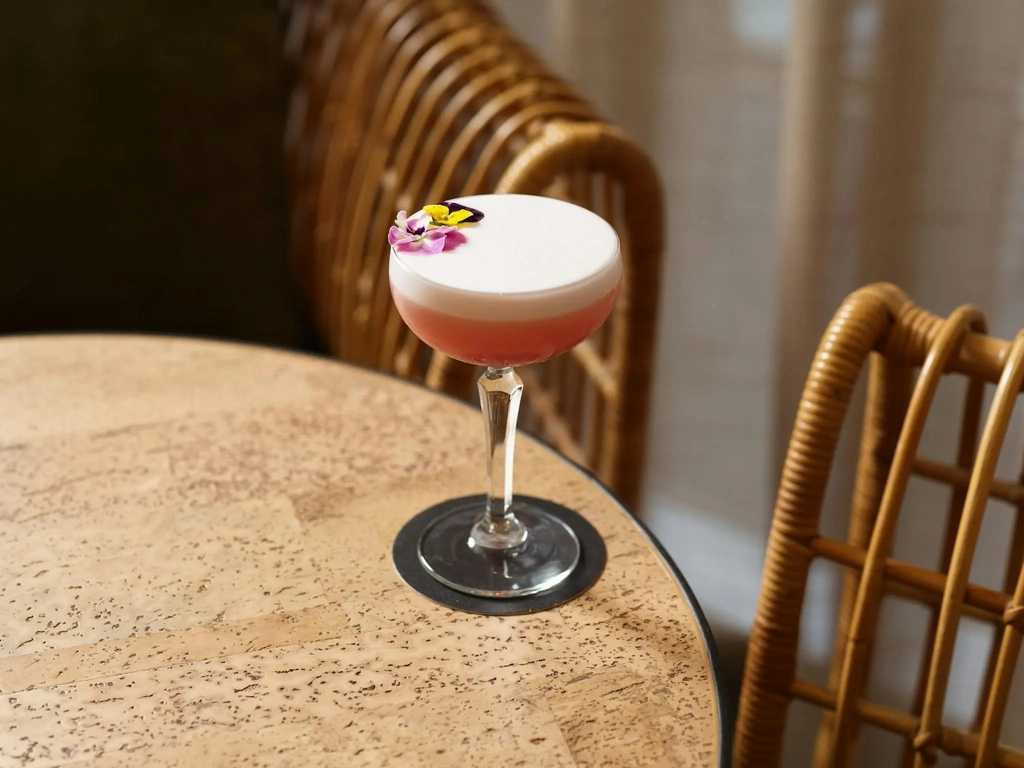 Pretty pink cocktail with floral decoration on a wooden round table in Hurricane's Surfers Paradise.