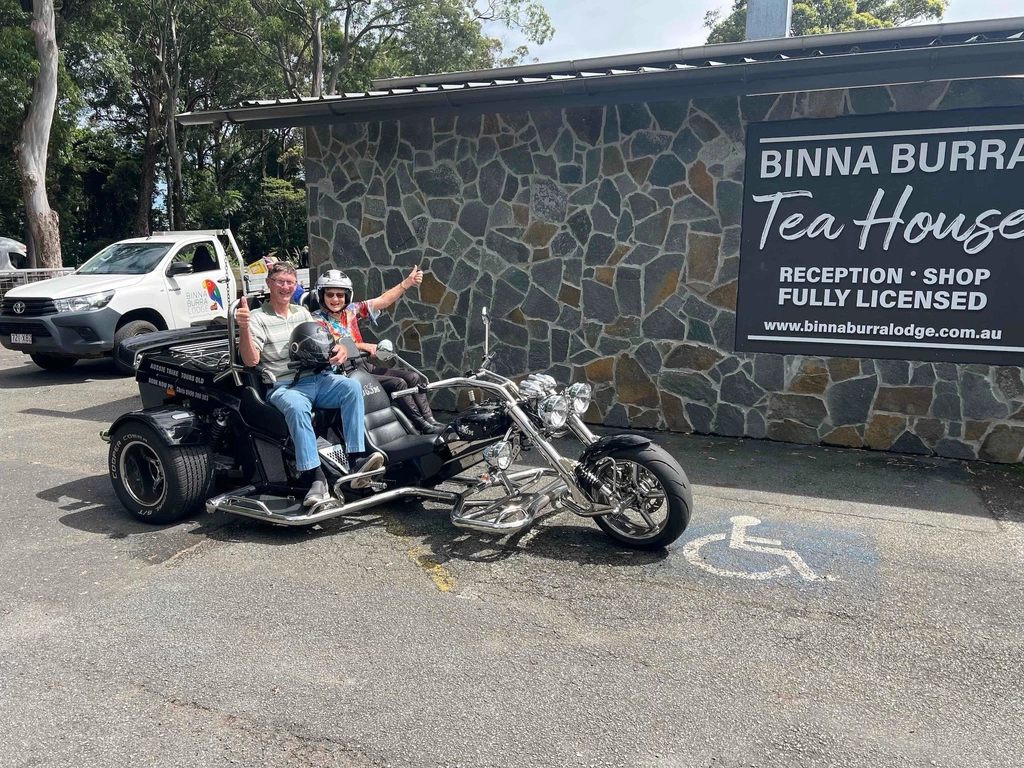 Image shows two passengers on the back of the trike in front of the Binna Burra Tea house.