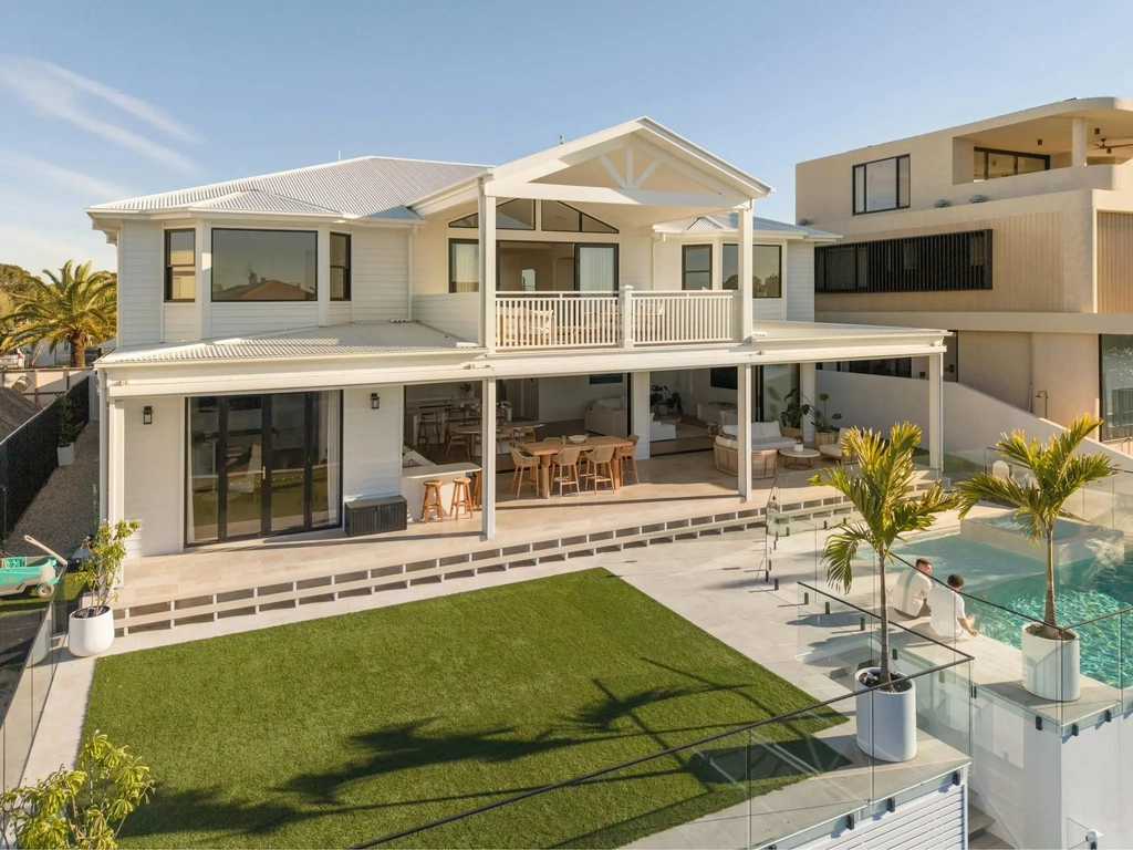Aerial view of a two storey white house with a pool, spa and lawn beside a canal