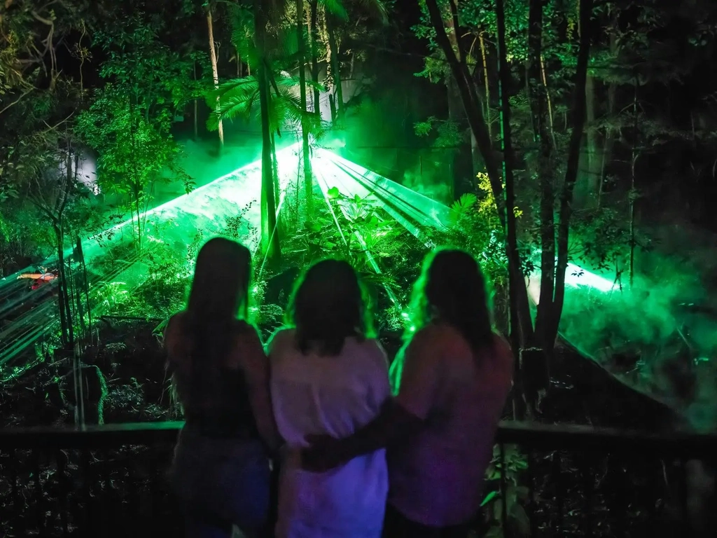Three people watching a green light spectacle in bushland.