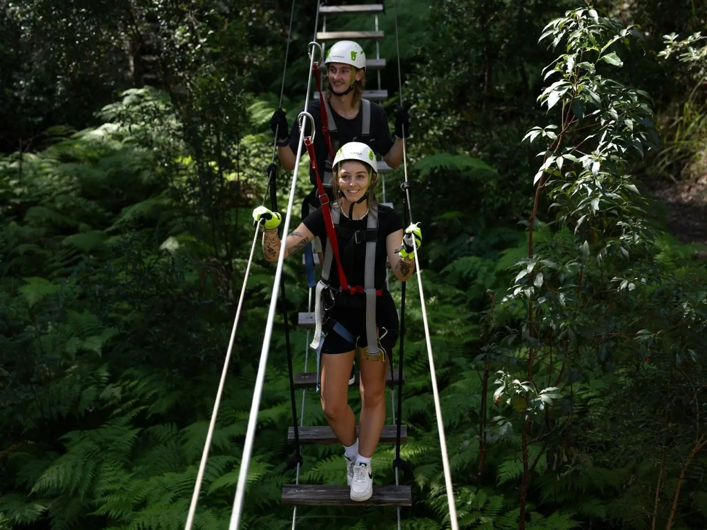 2 people walking across a suspension bridge smiling.