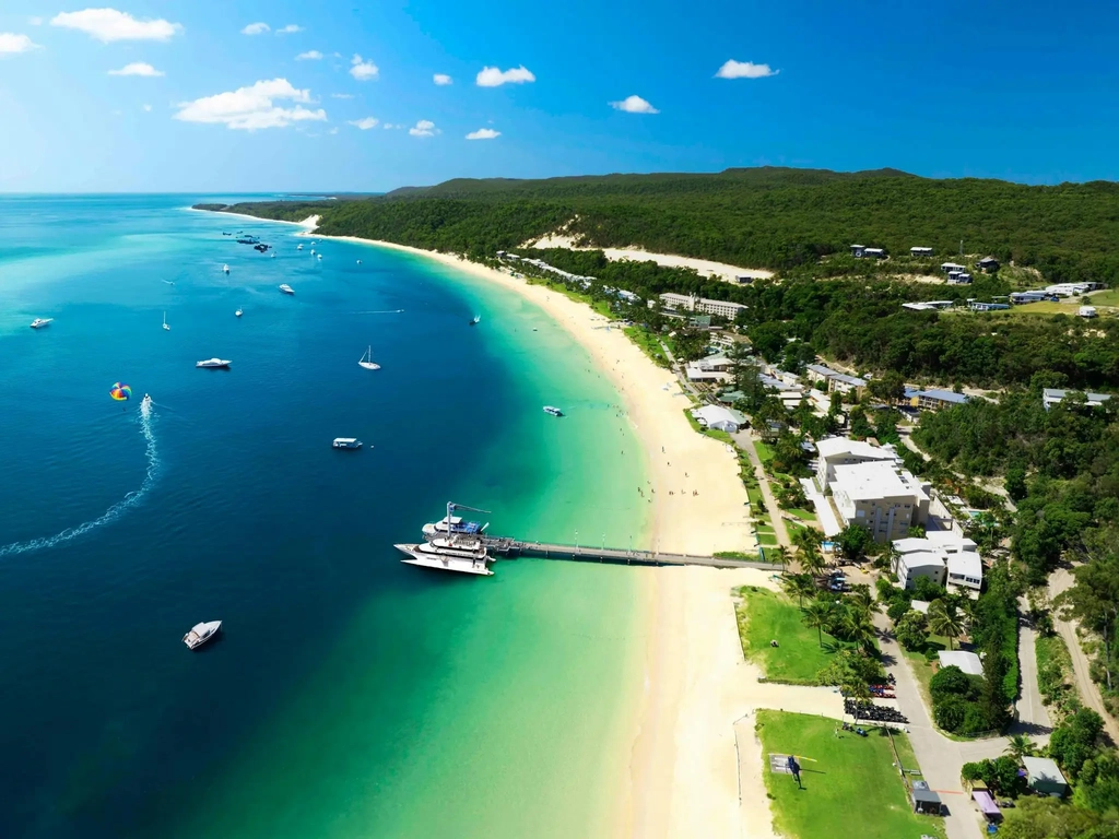 Boat at a jetty and a resort situated on a sandy beach and turquoise water